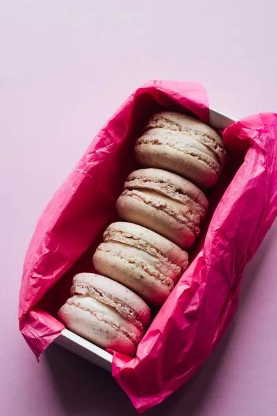 delicious colorful macaroons in pink paper box on lilac background, sweet dessert