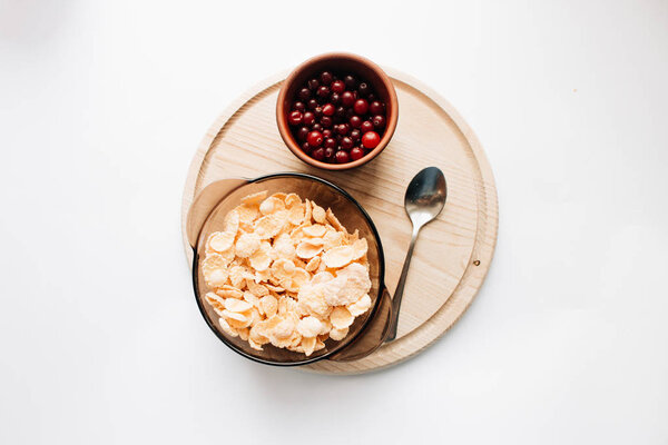 cranberries, crisp bread and delicious crispy cornflakes in bowl on wooden board over white background,  healthy breakfast