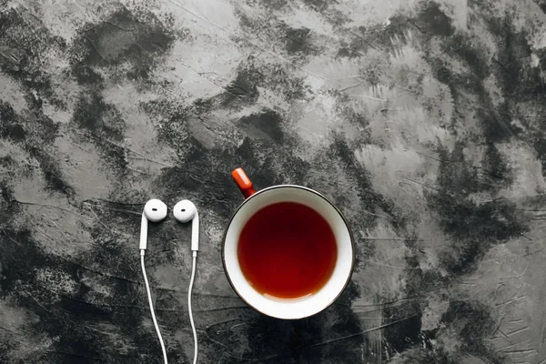 white modern earphones and cup of tea on black stone background