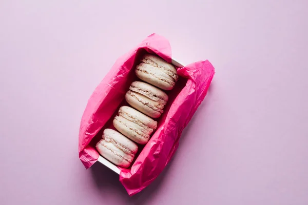 delicious colorful macaroons in pink paper box on lilac background, sweet dessert