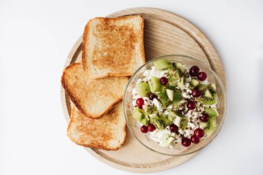 delicious cottage cheese with kiwi pieces and cranberries in bowl and toasts on wooden board clipart