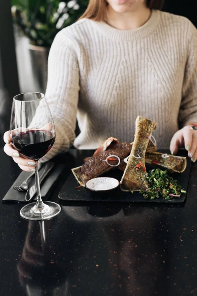 woman eating delicious roasted meat and drinking red wine