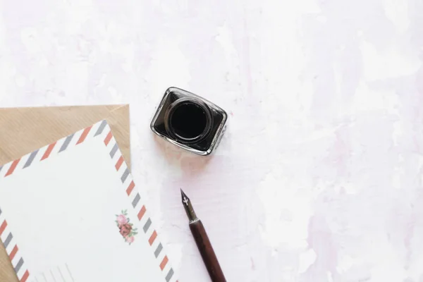 set of vintage dip pen, inkpot, blank paper sheet and envelope on white wooden table