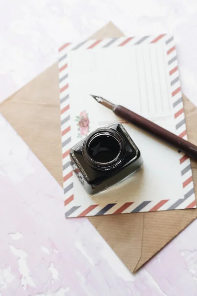 set of vintage dip pen, inkpot, blank paper sheet and envelope on white wooden table