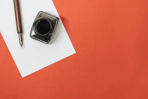 Set of vintage dip pen, inkpot and blank paper sheet on red background