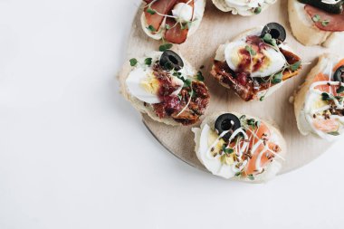 Yumurtalı, somonlu, zeytinli ve etli nefis bruschettalar geleneksel İtalyan mutfağı, beyaz masadaki malzemeler.
