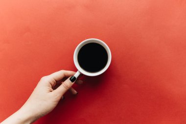 female hand holding cup of coffee on red background 