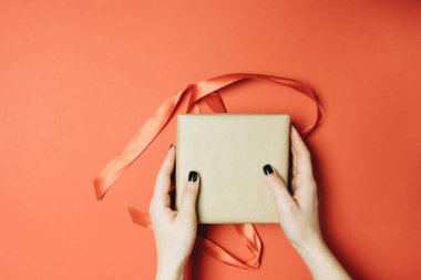 Kırmızıda izole edilmiş hediye kutusuna kurdele bağlayan kadının kısmi görüntüsü