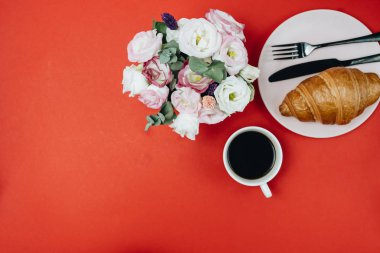 Üzerinde çiçekler ve kruvasan olan bir fincan kahvenin üst görüntüsü, kırmızı arka plan.