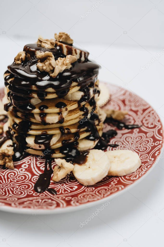 Stack of delicious homemade pancakes with chocolate topping, walnuts and sliced bananas