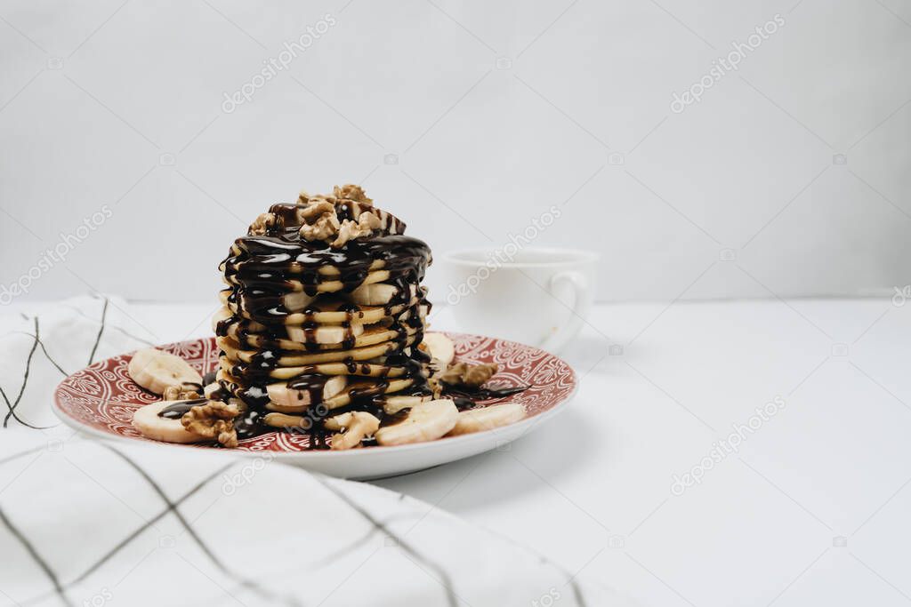 Stack of delicious homemade pancakes with chocolate topping, walnuts and sliced bananas