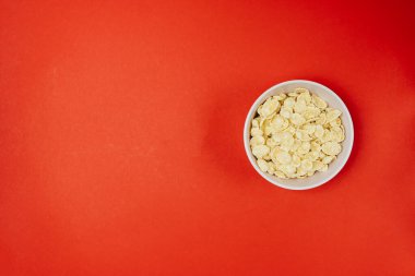 Kırmızı arka planda kasede mısır gevreği ve sağlıklı bir kahvaltı.