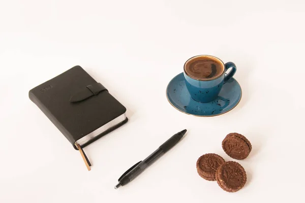 blue cup of coffee,notebook,pencil and brown biscuits on the white background