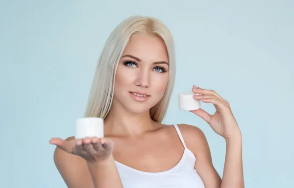 Girl or woman with clear skin and blue eyes keep on hands two white jar with cream and choose cream