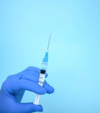 Doktor elinde şırınga tutuyor. İlaç enjeksiyonu. Mavi eldivenli bir tıp çalışanı. Şırıngada aşı. Kozmetik prosedürleri. Hemşire iğneyi yapacak.