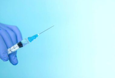 Doktor elinde şırınga tutuyor. İlaç enjeksiyonu. Mavi eldivenli bir tıp çalışanı. Şırıngada aşı. Kozmetik prosedürleri. Hemşire iğneyi yapacak.