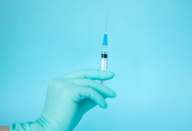 Doktor elinde şırınga tutuyor. İlaç enjeksiyonu. Mavi eldivenli bir tıp çalışanı. Şırıngada aşı. Kozmetik prosedürleri. Hemşire iğneyi yapacak.