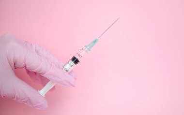 Doktor elinde şırınga tutuyor. İlaç enjeksiyonu. Pembe eldivenli bir tıp çalışanı. Şırıngada aşı. Kozmetik prosedürleri. Hemşire iğneyi yapacak.