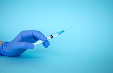 Doktor elinde şırınga tutuyor. İlaç enjeksiyonu. Mavi eldivenli bir tıp çalışanı. Şırıngada aşı. Kozmetik prosedürleri. Hemşire iğneyi yapacak.