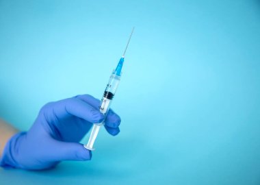 Doktor elinde şırınga tutuyor. İlaç enjeksiyonu. Mavi eldivenli bir tıp çalışanı. Şırıngada aşı. Kozmetik prosedürleri. Hemşire iğneyi yapacak.