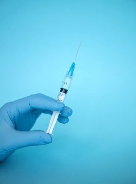 Doktor elinde şırınga tutuyor. İlaç enjeksiyonu. Mavi eldivenli bir tıp çalışanı. Şırıngada aşı. Kozmetik prosedürleri. Hemşire iğneyi yapacak.