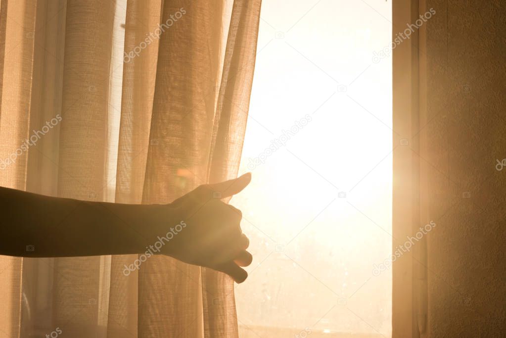 Female arm reaching out to open a curtain - warm sun light shining through. Mystery, new possibilities. Background.