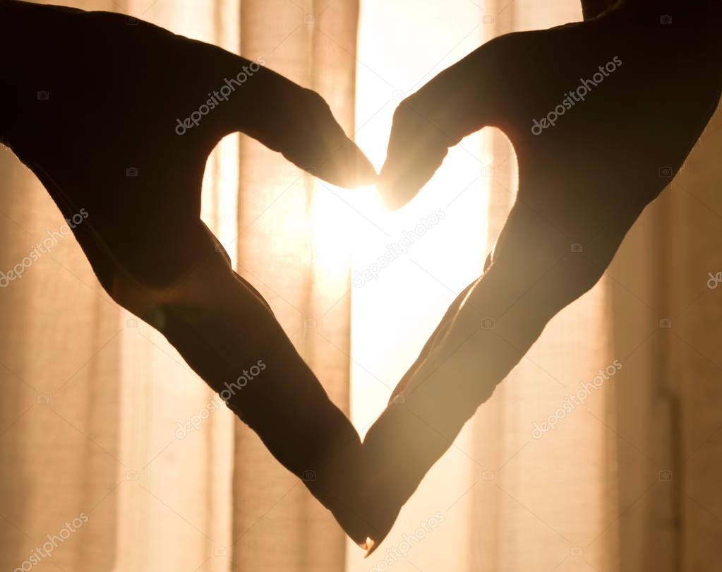 Beautiful heart made from hands, with warm light shining through curtains