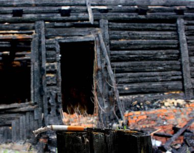 yanmış bir ahşap ev, dikkatsiz bir sigara kullanımı ile ateş izmarit arka planda