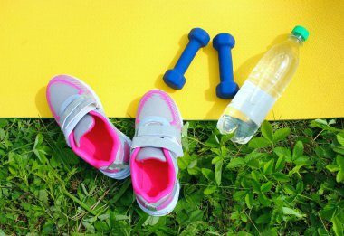 Halı dambıl, bir şişe su ve taze yeşil çim açık havada spor ayakkabıları ile sarı