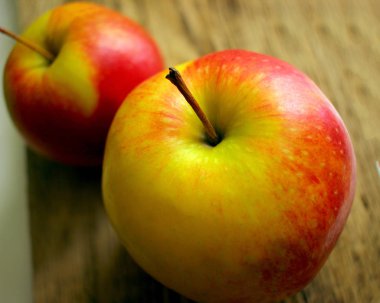 Eski ahşap bir masanın arka planında iki sulu olgun elma.