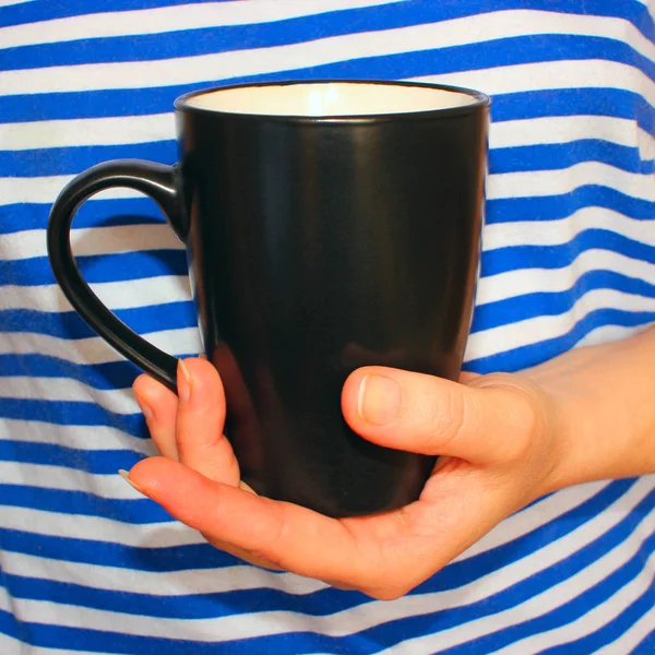 在条纹衬衫背景上的一大杯咖啡 在女性手中 — 图库照片