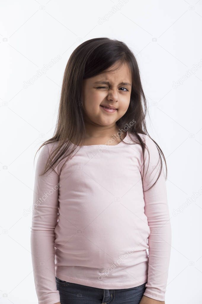 Little girl in pink top and jeans winking her eye standing against a white background.