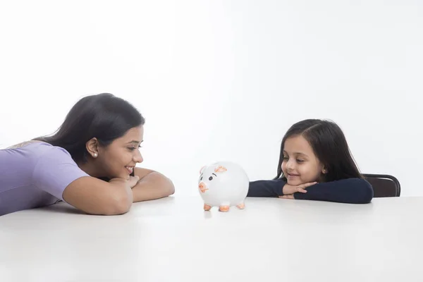 Mother Daughter Leaning Table Looking Piggy Bank — Stock Photo, Image