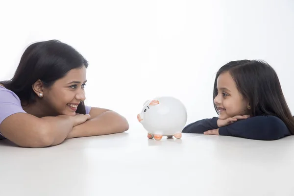 Happy Mother Daughter Leaning Table Looking Piggy Bank — Stock Photo, Image