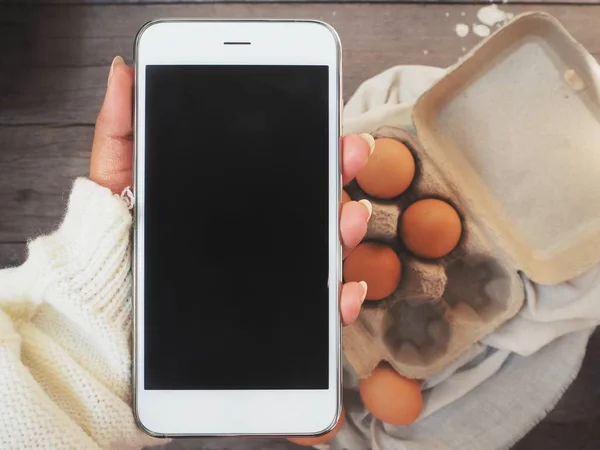 Smart phone on hand with eggs in box