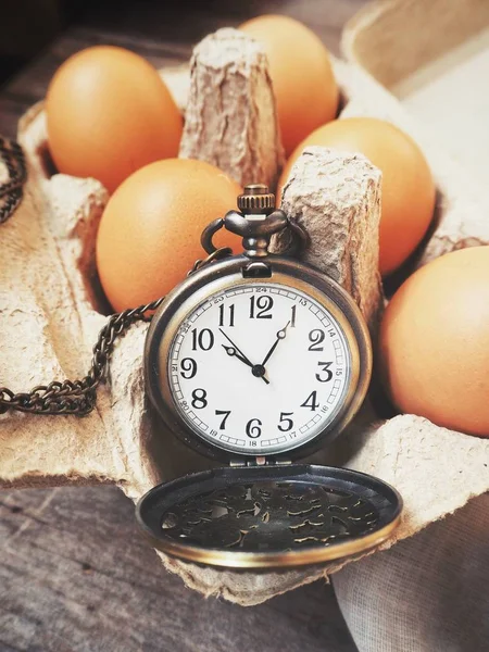 Яйця в коробці з старовинним кишеньковим годинником — стокове фото
