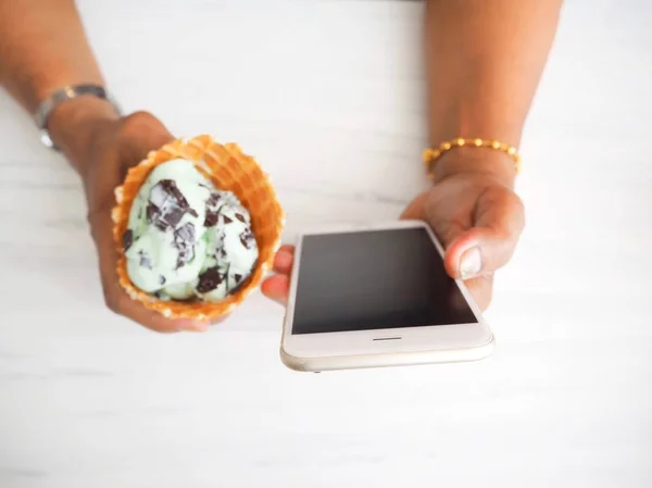 Mulher comendo sorvete de hortelã com telefone inteligente — Fotografia de Stock