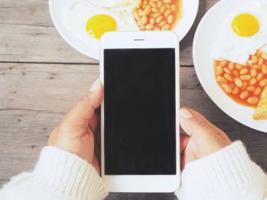 İngiliz kahvaltısı ile akıllı telefon kullanan kadın