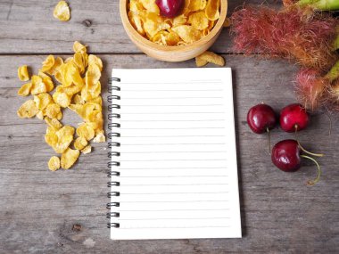 Mısır gevreği Kiraz ahşap arka plan üzerinde boş not defteri ile yalan ile