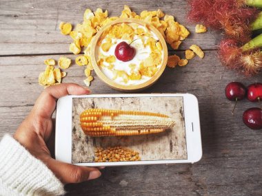 Mısır gevreği ile smartphone ahşap arka plan üzerinde kadın alarak fotoğraf