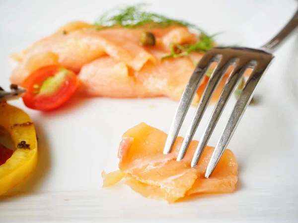 close up of edible smoked salmon and fork on plate
