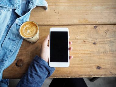 Akıllı telefon ve kahve fincanı masaya kullanan kadın