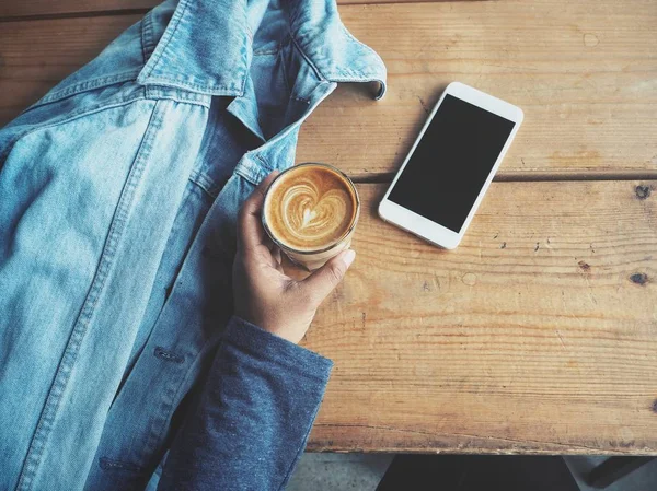 Akıllı telefon ve kahve fincanı masaya kullanan kadın