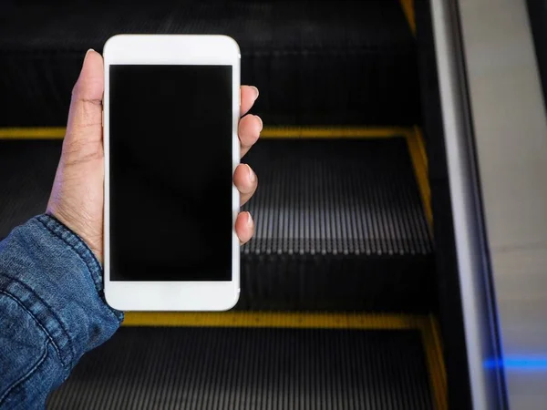 Teléfono inteligente a mano con escaleras mecánicas en el centro comercial — Foto de Stock