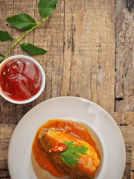 Eski ahşap arka plan üzerinde domates soslu beyaz tabakta konserve balık