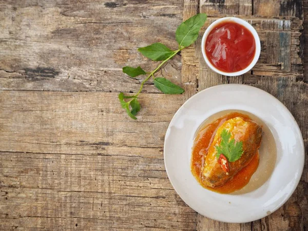 Eski ahşap arka plan üzerinde domates soslu beyaz tabakta konserve balık