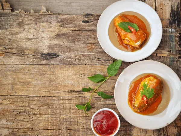 Eski ahşap arka plan üzerinde domates soslu beyaz tabaklarda konserve balık