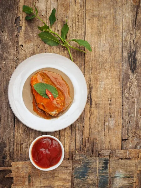 Eski ahşap arka plan üzerinde domates soslu beyaz tabakta konserve balık