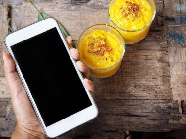 Kadın holding smartphone geleneksel Hint yakınındaki içecek Mango lassi ahşap arka plan üzerinde