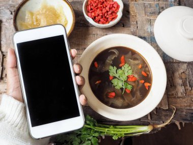 Köpekbalığı yüzgeci ahşap arka plan üzerinde ile kadın yandan Çin çorbası ile Smartphone